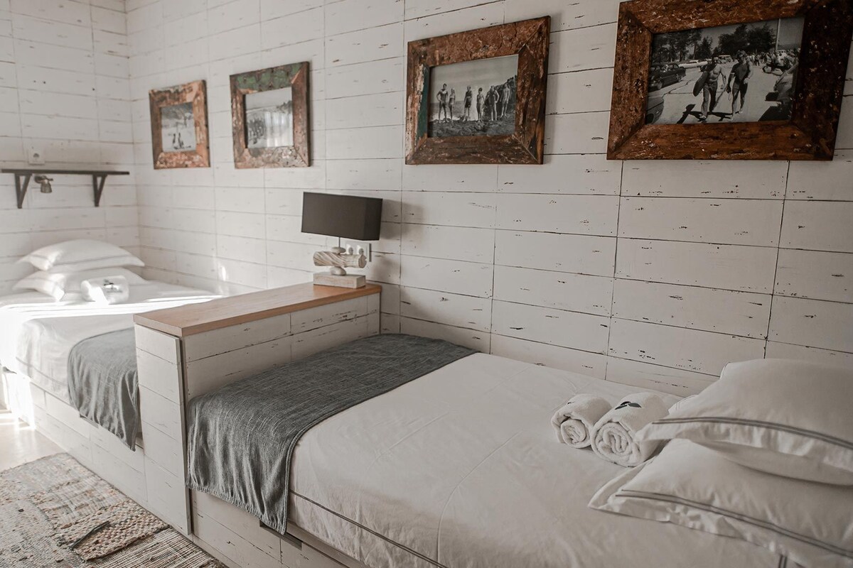 A bedroom with two beds, a bedside table, a TV, and framed pictures on the wall.