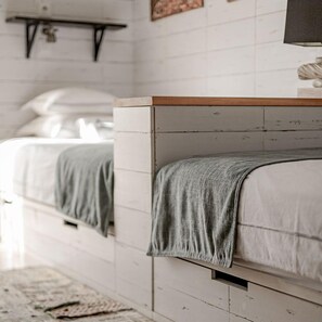 A bedroom with two beds, a wooden headboard, a white wall, and a small shelf above the beds. - Surfers Lodge Peniche (Peniche)