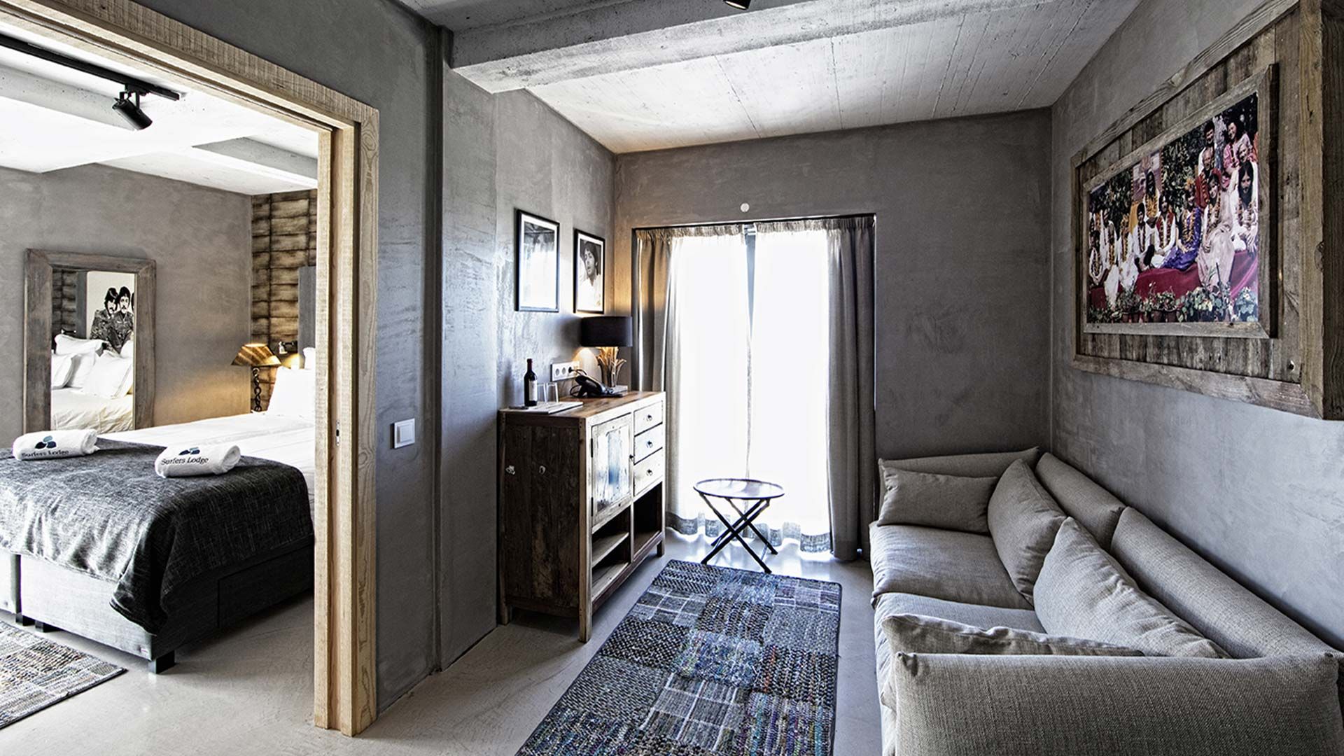 A modern hotel room with a bed, a sofa, a small table, and a painting on the wall.