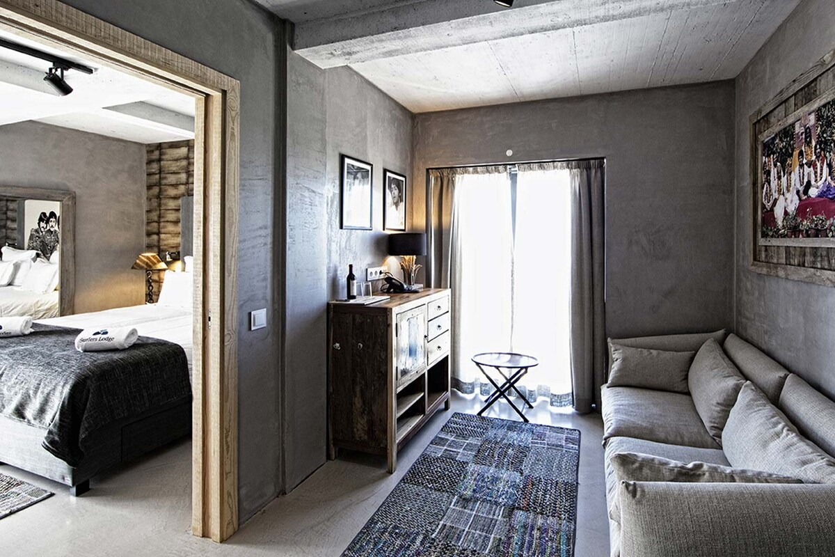 A modern hotel room with a bed, a sofa, a small table, and a painting on the wall.