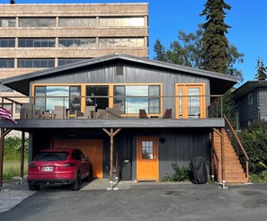 Une maison moderne à deux étages, dotée d’un garage, avec une voiture rouge garée devant et un escalier menant à l’étage supérieur.