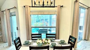A dining area with a table set for four, chairs with striped cushions, a chandelier, and a view through a large window. - Luxurious Relaxation Home - Pool Games / 8PPL-4BR (Tampa)