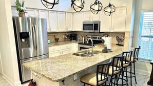 A modern kitchen with white cabinets, stainless steel appliances, a granite countertop, and pendant lighting. - Luxurious Relaxation Home - Pool Games / 8PPL-4BR (Tampa)