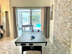 Relax in a spacious room with a foosball table and sliding glass door leading to a pool and patio area.