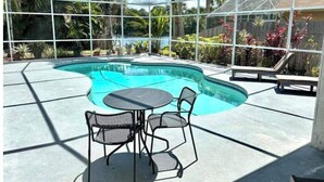 A covered outdoor swimming pool with a table and chairs, surrounded by tropical plants and a wooden fence. - Luxurious Relaxation Home - Pool Games / 8PPL-4BR (Tampa)