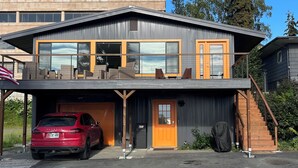 A modern two-story house with a garage, a red car parked in front, and a staircase leading to the upper level. - Waterfront unit! Walk to shops, dining, & trails! (Anchorage)