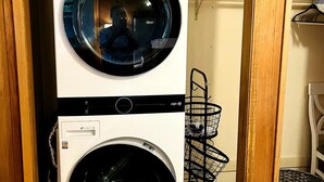 A laundry room with two stacked washing machines, a metal rack, and a wicker basket. - Waterfront unit! Walk to shops, dining, & trails! (Anchorage)