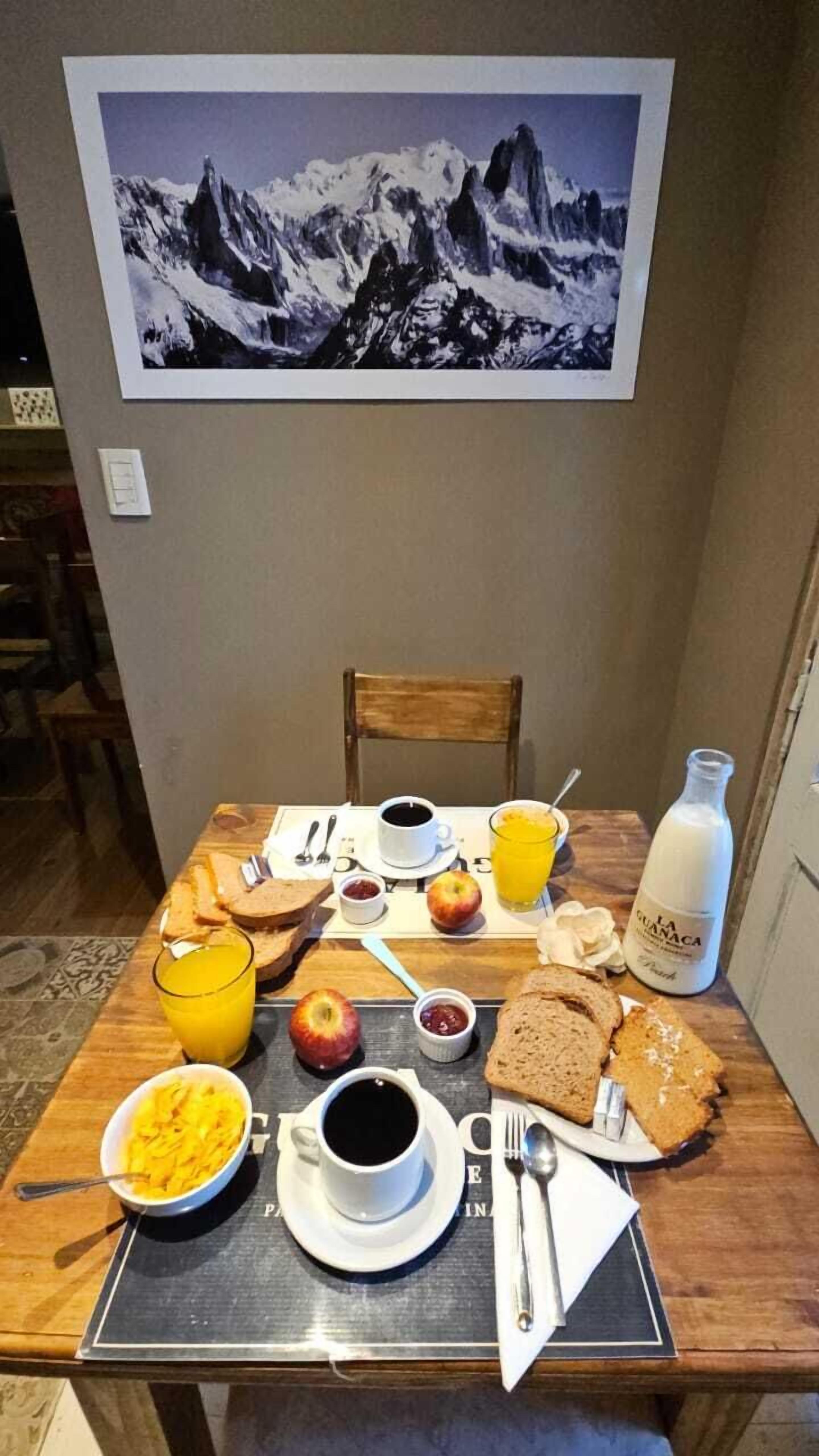 A breakfast setup with toast, fruit, coffee, and juice on a table, with a mountain painting above.