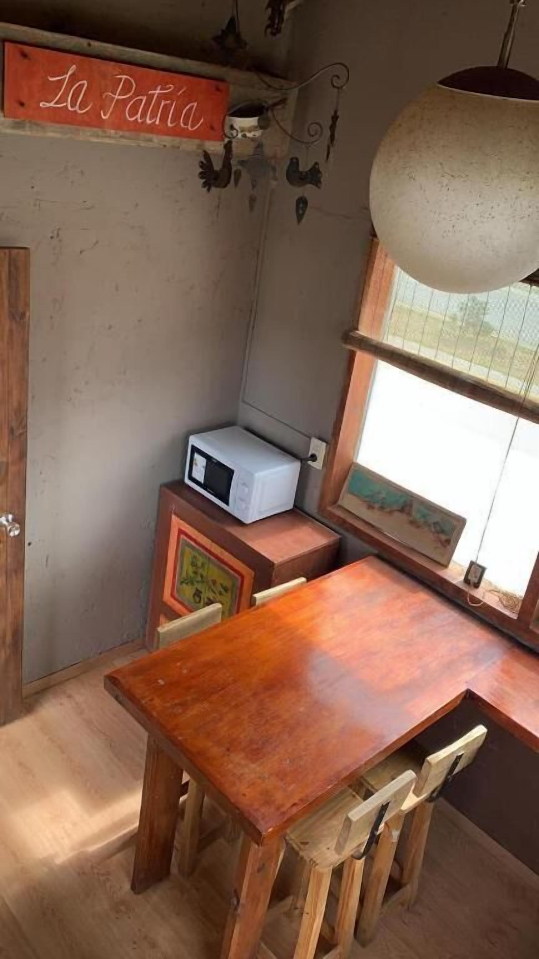 A small, rustic kitchen with a wooden table and chairs, a microwave, and a hanging light fixture.