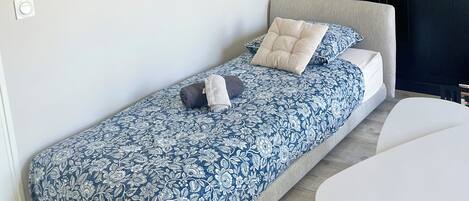 Una stanza moderna e accogliente con un letto singolo, un tavolo bianco e un grande quadro astratto appeso al muro.
