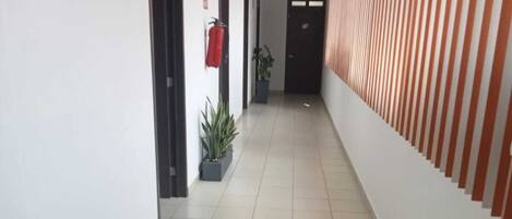 A corridor with tiled flooring, potted plants, and a fire extinguisher on the wall.