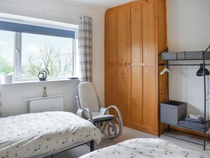 A bedroom with a bed, a chair, a wardrobe, a radiator, a window with curtains, and a view of trees outside. - 2 bedroom accommodation in Aspatria (Aspatria)