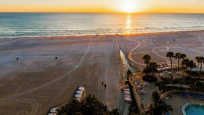 Ein Strand mit Poolbereich, Liegestühlen und Blick auf den Sonnenuntergang.