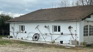 A white building with a tiled roof, a large wheel, and potted plants. - Club House Dans Mini Ferme Danimation et Refuge (Courlans)