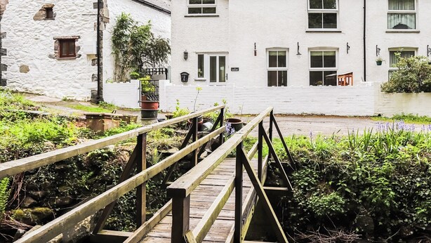 Ein weißes Gebäude mit einer steinernen Fassade, einer Holzbrücke und einem Garten.