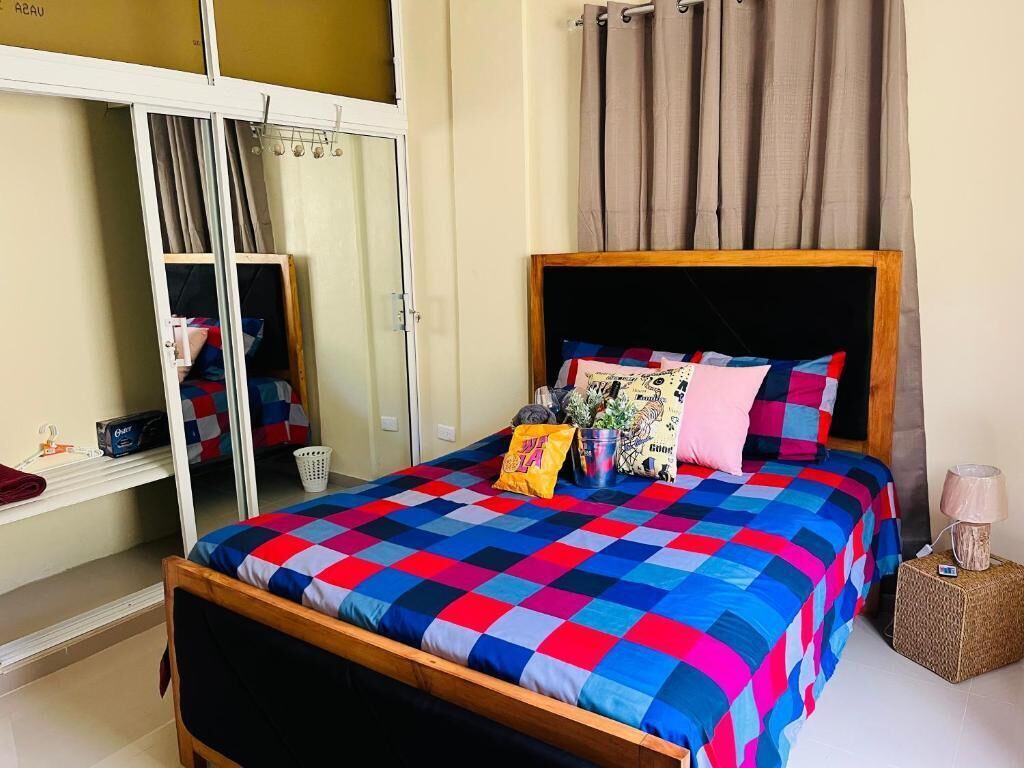 A bedroom with a bed, a wardrobe, a mirror, a lamp, and a curtain.