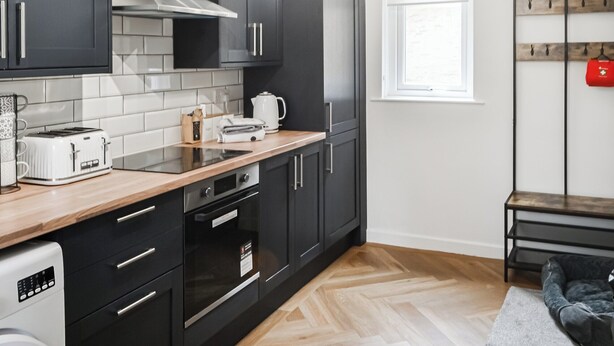 Una cocina moderna con armarios oscuros, encimera de madera, horno empotrado y cafetera.