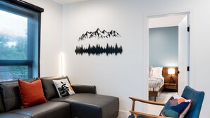 Ein modernes Wohnzimmer mit einem schwarzen Ledersofa, einem Holzstuhl und einer Wandsticker-Motiv von Bergen.