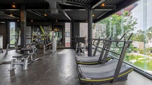 A modern gym with treadmills, weight machines, and a large window overlooking a garden.