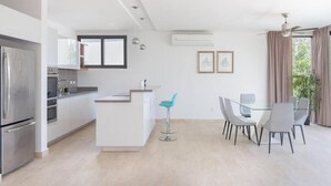 A modern kitchen with a central island, a dining area with a glass table and chairs, and a large window with curtains.