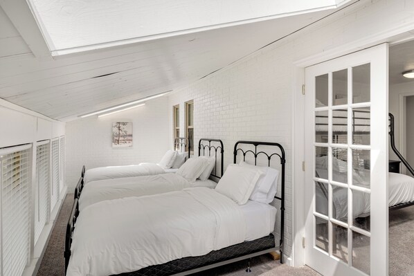 A bedroom with two beds, white bedding, a white brick wall, and a skylight. - The Hideaway | 3 RV Hookups | Sleeps 17+ (Garden City)