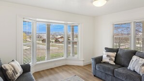 A room with a corner window, a grey sofa, and a white ceiling. - The Hideaway | 3 RV Hookups | Sleeps 17+ (Garden City)