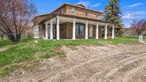 A two-story brick house with a covered porch and a large tree in the yard. - The Hideaway | 3 RV Hookups | Sleeps 17+ (Garden City)
