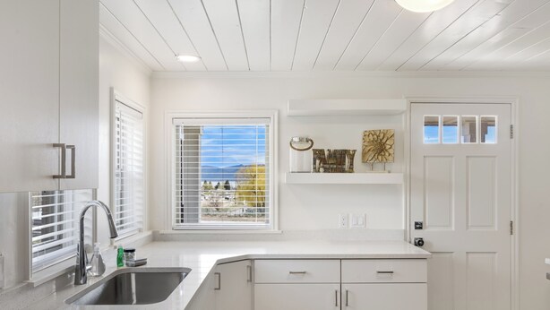 A kitchen with white cabinets, a stainless steel sink, and a window with blinds. - The Hideaway | 3 RV Hookups | Sleeps 17+ (Garden City)
