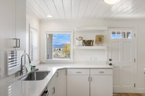 A kitchen with white cabinets, a stainless steel sink, and a window with blinds. - The Hideaway | 3 RV Hookups | Sleeps 17+ (Garden City)