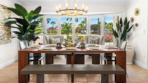 A dining area with a large wooden table, multiple chairs, and a chandelier. There are large windows providing a view of the outdoors. - Sunset Villa - Htd Salt Pool - Hot Tub -Canal-Golf (Cape Coral)