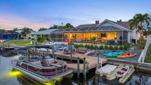 A waterfront property with a dock, a boat, and a house with outdoor seating and a pool. - Sunset Villa - Htd Salt Pool - Hot Tub -Canal-Golf (Cape Coral)