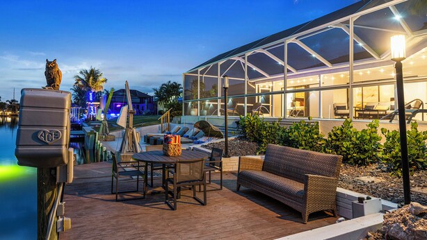 A modern outdoor deck with a glass-enclosed area, a pool, and lounge furniture. - Sunset Villa - Htd Salt Pool - Hot Tub -Canal-Golf (Cape Coral)