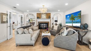 A spacious living room with a fireplace, a dining area, and a kitchen visible through an open doorway. - Sunset Villa - Htd Salt Pool - Hot Tub -Canal-Golf (Cape Coral)
