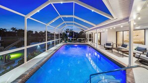 A swimming pool with a glass enclosure, lounge chairs, and a view of the surrounding area. - Sunset Villa - Htd Salt Pool - Hot Tub -Canal-Golf (Cape Coral)