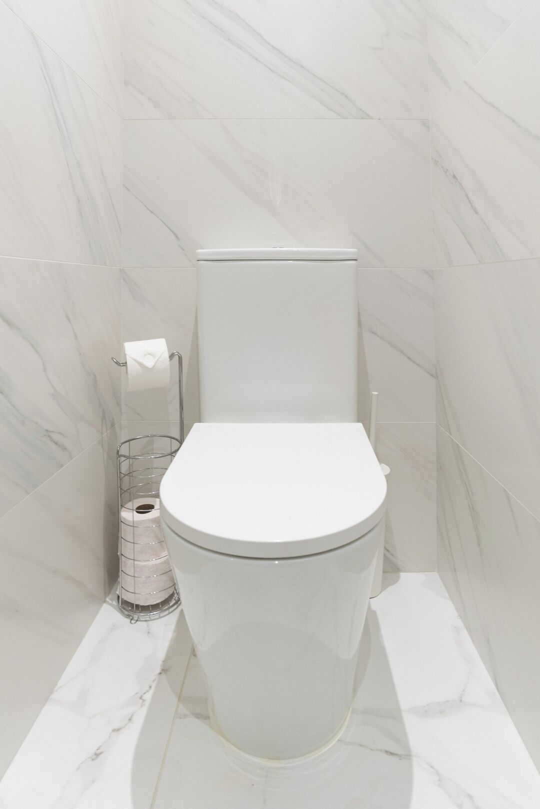 Un baño moderno con inodoro blanco, paredes de mármol y suelo de mármol.