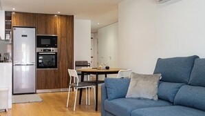 Un salon moderne avec un canapé bleu, une table à manger avec des chaises et un coin cuisine équipé d’appareils électroménagers.