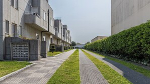 Un immeuble résidentiel moderne avec un chemin rectiligne, une haie bien entretenue et un ciel dégagé.