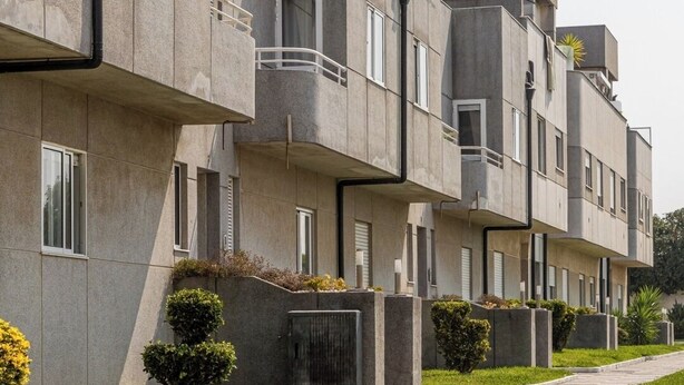 Un immeuble d’appartements moderne doté de balcons, d’une allée pavée et de petits espaces paysagers.
