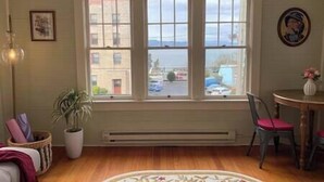 A room with a large window, a radiator, a chair, and a small table with a vase. - The Historic Downtown Astoria Flats (Astoria)