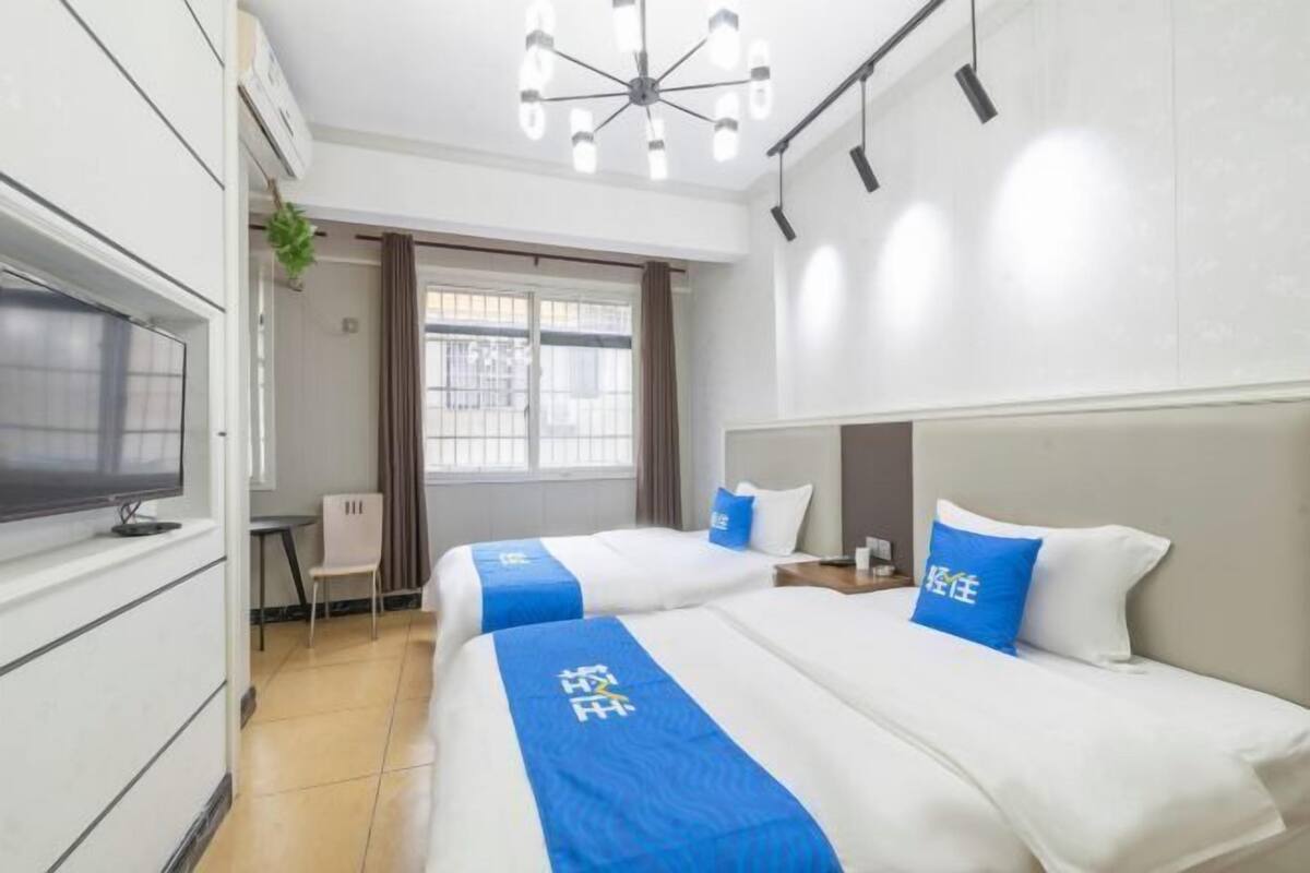 A hotel room with two beds, a TV, a desk, and a window with curtains.