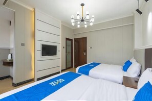 Une chambre d’hôtel avec deux lits, une télévision, un minibar et un lustre.