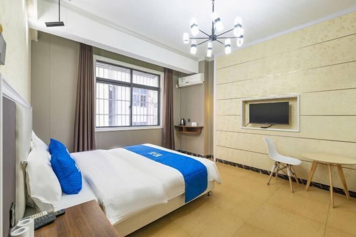 A hotel room with a bed, a desk, a chair, a TV, and a window.