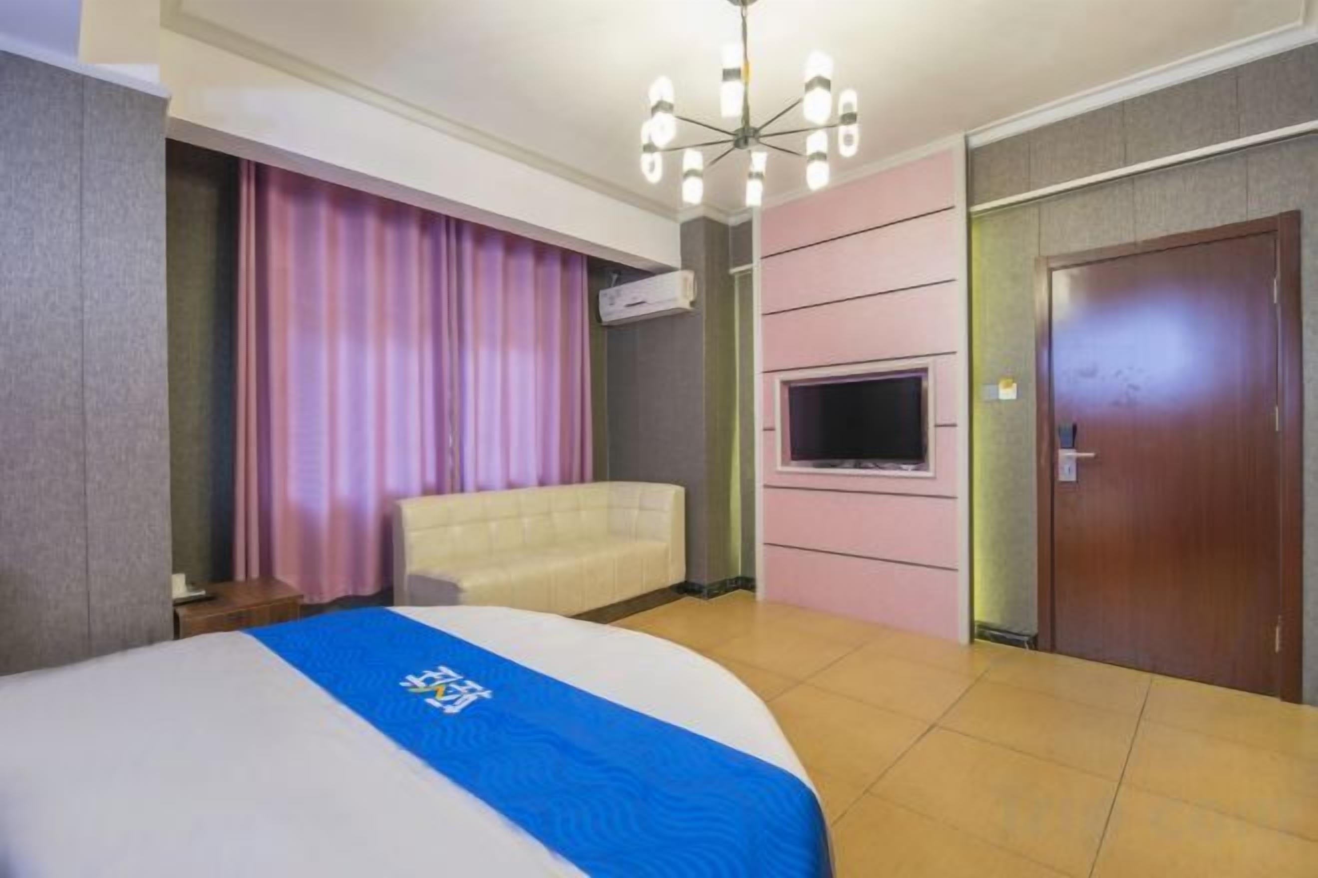 A hotel room with a bed, a television, a sofa, and a door.