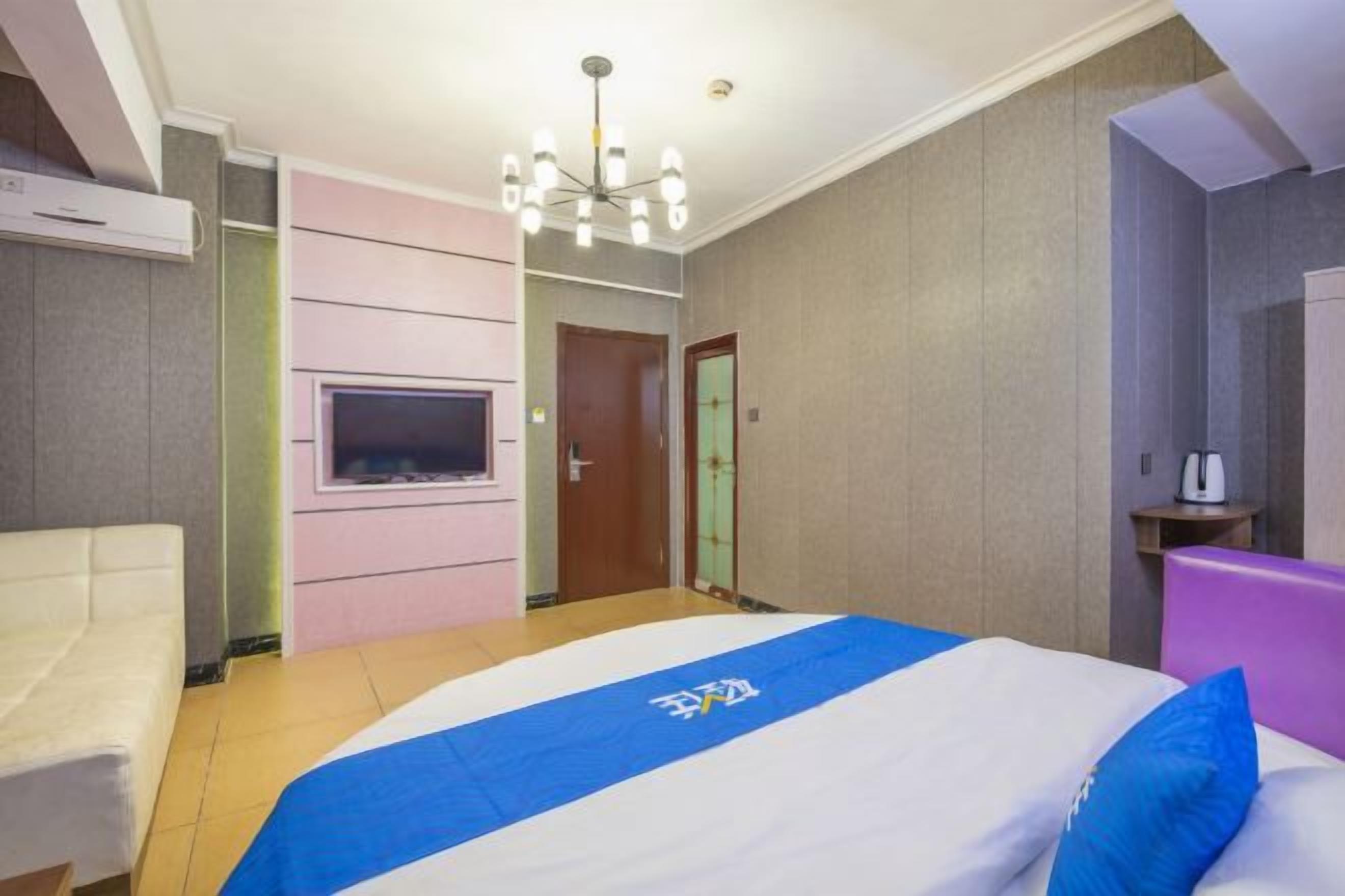 A hotel room with a bed, a chair, a TV, and a door.
