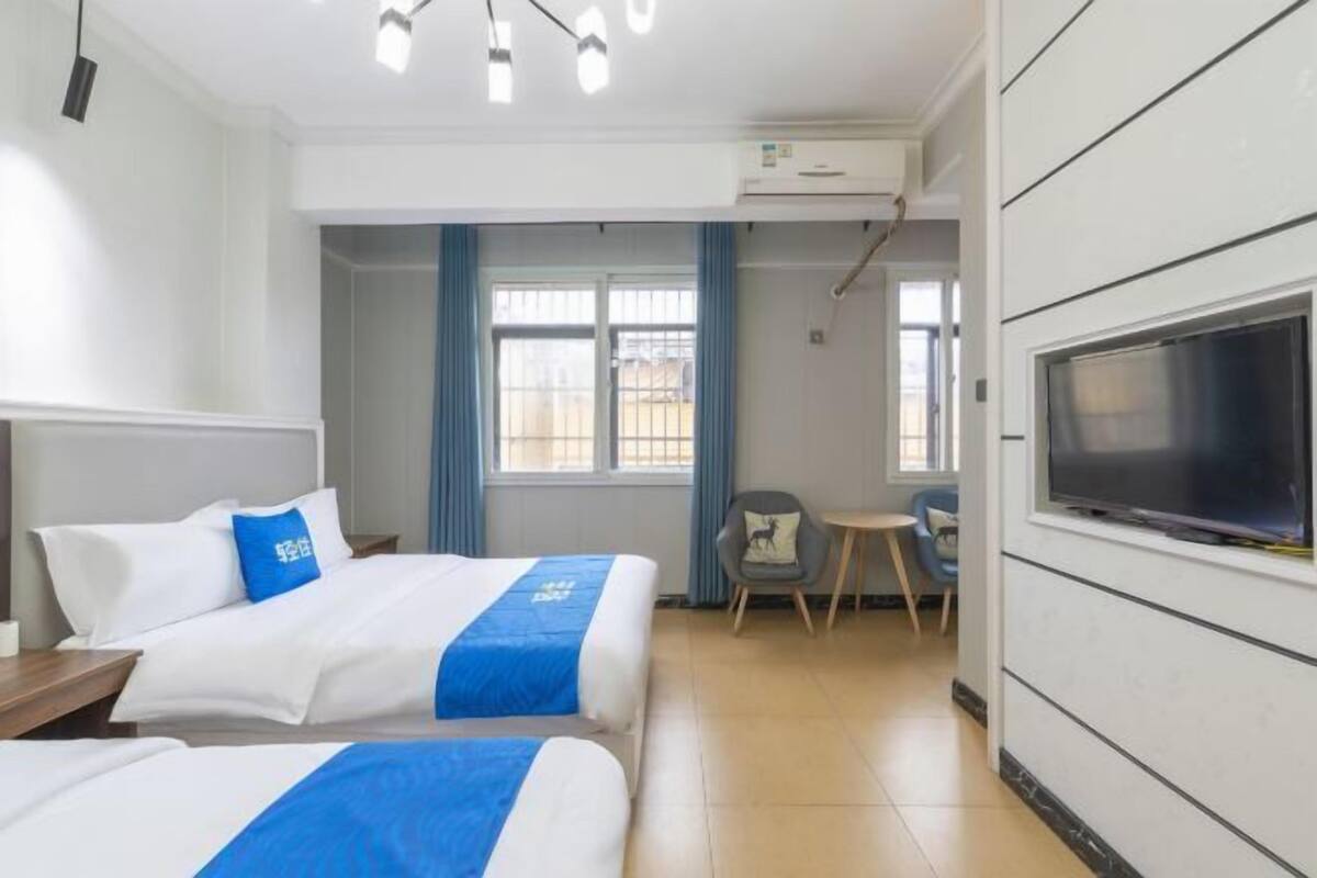 A hotel room with two beds, a TV, a small table, and a chair.