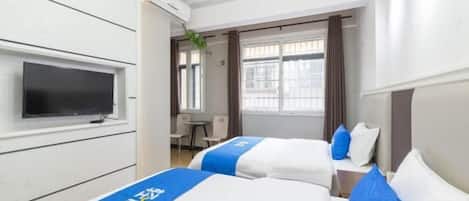 Ein Hotelzimmer mit zwei Betten, einem Flachbildfernseher, einem Schreibtisch und einem Vorhangfenster.