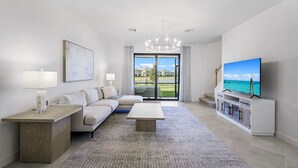 A modern living room with a sofa, coffee table, TV, and a view of a green landscape through the glass door.