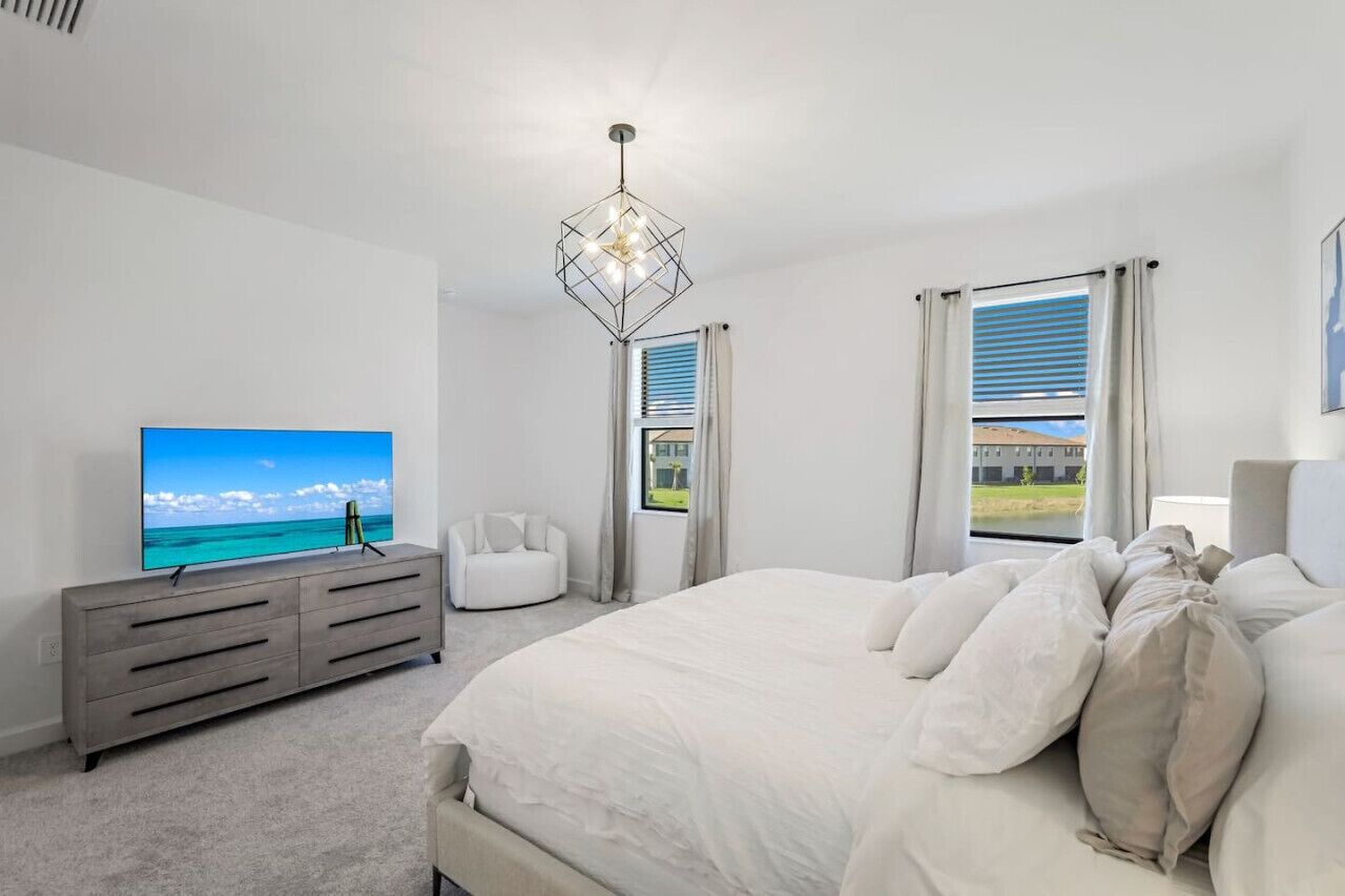 A bedroom with a bed, a TV on a dresser, and a view of the outdoors through a window.
