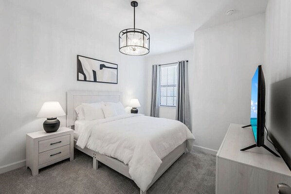 Un dormitorio moderno con cama, mesitas de noche, televisor y candelabro.