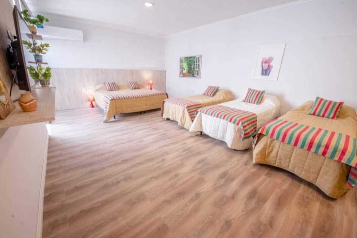 A hotel room with four beds arranged in a row, a wooden floor, and a small desk with a plant.